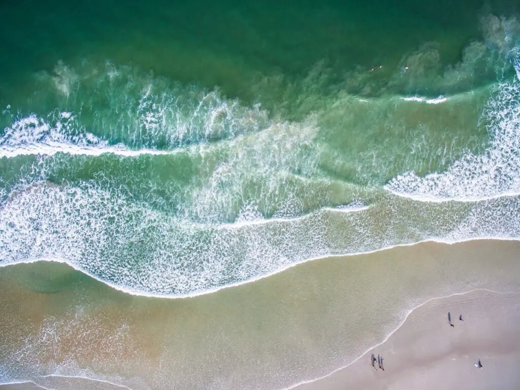 A beach with people walking on it and waves coming in