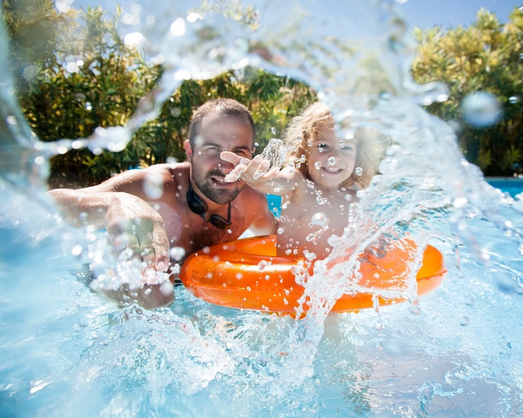 A man and child in the water on an inflatable raft.