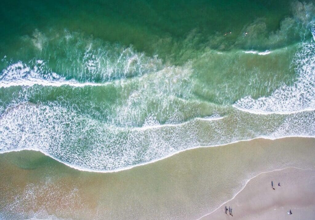 A beach with people walking on it and waves coming in